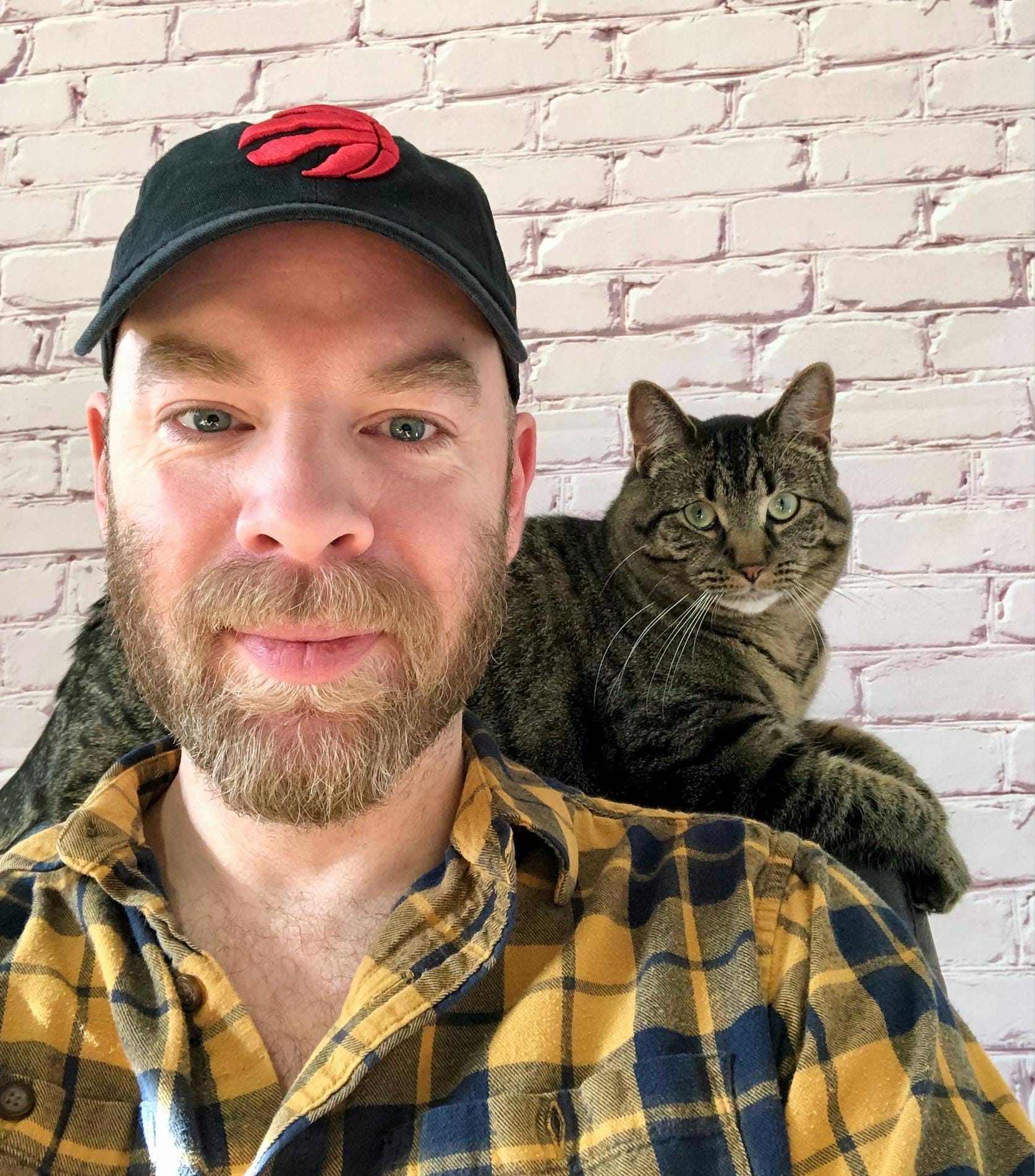The man is looking into the camera and has his cat on his shoulders.
